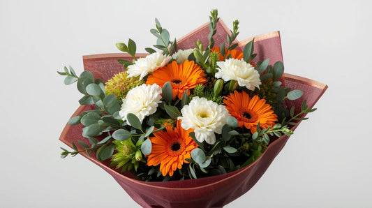 Bouquet of flowers with orange and white flowers wrapped in brown paper on a light gray background