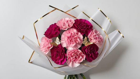 A bouquet of pink and purple carnations wrapped in white paper with gold accents.