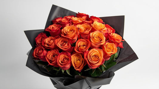 Bouquet of red and orange roses wrapped in black paper on a light gray background