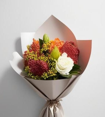 A bouquet of flowers wrapped in paper, featuring a variety of colors and types of flowers.