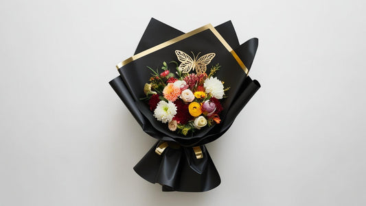 Bouquet of flowers wrapped in black paper with gold accents on a white background