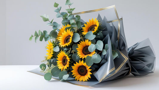 Bouquet of sunflowers wrapped in gray paper with gold accents on a light background