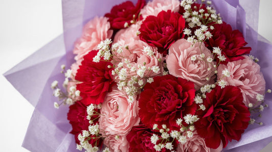 Bouquet of red and pink flowers with white accents on a light purple background