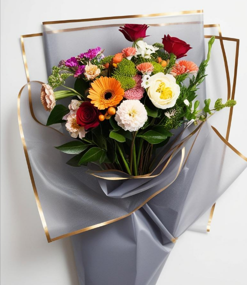 Bouquet of colorful flowers wrapped in gray paper with gold trim on a light gray background